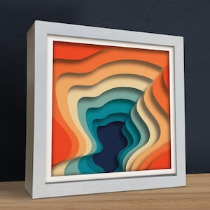 Könnte beinhalten: Ein gerahmter abstrakter Kunstdruck mit einem mehrschichtigen, ausgeschnittenen Papierdesign. Das Design zeigt eine Reihe von sich überlappenden, geschwungenen Formen in Orange-, Gelb-, Blau- und Grüntönen, die ein Gefühl von Tiefe und Dimension erzeugen.