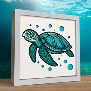 Puede incluir: Una obra de arte enmarcada con una ilustración de una tortuga marina turquesa. La tortuga está representada con patrones detallados y rodeada de burbujas turquesas sobre un fondo blanco. La obra de arte está encerrada en un marco blanco, con una escena submarina borrosa en el fondo.