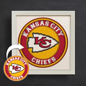 May include: A framed print of the Kansas City Chiefs logo. The logo is a red circle with a yellow arrowhead inside. The words "Kansas City Chiefs" are written around the circle.
