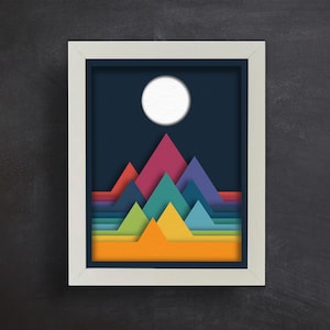 May include: A framed print of a colorful abstract mountain landscape with a white circle in the sky. The mountains are layered in shades of blue, green, yellow, orange, and red.