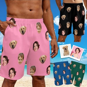 May include: Pink shorts featuring a repeating pattern of various human faces and golden retriever dog faces. The design includes multiple distinct portraits scattered across the fabric, showcasing a personalized graphic print on the garment.
