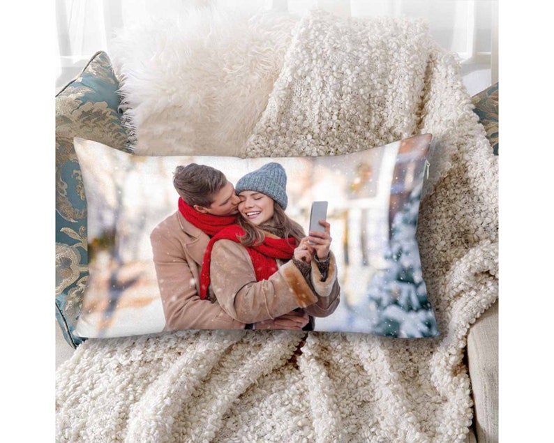 K&ouml;nnte beinhalten: Ein wei&szlig;es Kissen mit einem gedruckten Bild eines Paares in einer verschneiten Umgebung. Das Paar tr&auml;gt Winterkleidung und h&auml;lt ein Telefon. Das Bild ist auf der Vorderseite des Kissens gedruckt.