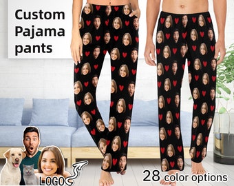 May include: Black pajama pants featuring a repeating pattern of small red hearts and multiple custom printed faces of a man and a woman. The text Custom Pajama pants is visible in the upper left corner and 28 color options is at the bottom.