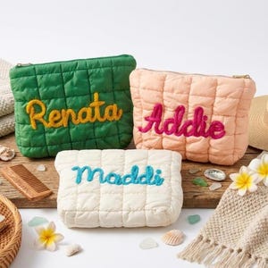 May include: Three quilted cosmetic bags in green, peach, and cream, each embroidered with a name in a contrasting colour. The green bag has "Renata" in yellow, the peach bag has "Addie" in pink, and the cream bag has "Maddi" in blue.