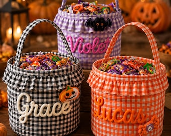 May include: Three fabric Halloween candy buckets with gingham patterns in black, purple, and orange. Each bucket features a ruffled top edge, a handle, and a personalized name in raised lettering: Grace, Violet, and Lucas, with small themed patches.