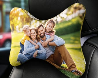 May include: A bone-shaped car headrest pillow featuring a full-color photographic print of a family of four sitting together on a grassy lawn. The pillow is attached to a black leather car seat and displays a smiling group in casual clothing.