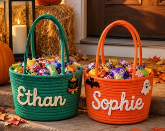 May include: Two round rope baskets filled with assorted candy. The green basket features the name Ethan in white script and a black cat patch. The orange basket features the name Sophie in white script with black bat and white ghost patches.