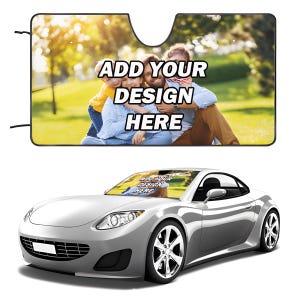 May include: A custom car windscreen sun shade featuring a printed photograph of a family in a park, with the bold black text ADD YOUR DESIGN HERE overlaid in the centre. The shade is shown installed in a silver sports car windscreen.