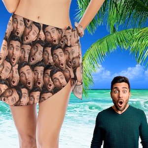 May include: A colorful sarong with a pattern of many faces. The sarong is tied around the waist and is worn by a person standing on a beach. The person is wearing a swimsuit. The background is a beach with blue water and a palm tree.