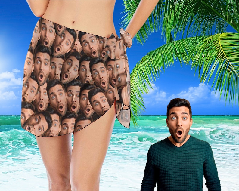 May include: A colorful sarong with a pattern of many faces. The sarong is tied around the waist and is worn by a person standing on a beach. The person is wearing a swimsuit. The background is a beach with blue water and a palm tree.