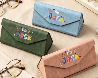 May include: Three triangular folding glasses cases in light blue, olive green, and dusty pink. Each case features the text "Mr. Jack" in colorful, patterned letters, accompanied by small graphic icons of hearts, pencils, and apples on the front flap.