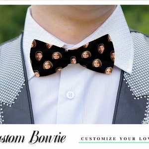 May include: A black bow tie with a repeating pattern of faces. The bow tie is worn by a person wearing a white shirt and a black suit jacket. The text "Custom Bowtie" and "Customize Your Love" is visible below the image.