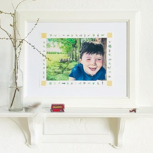 May include: Framed illustration of a young boy smiling, peeking out from behind a tree in a woodland setting. The illustration is surrounded by a border of small, colourful nature-themed icons.