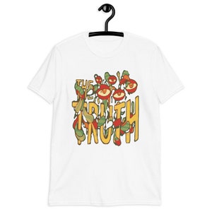 Puede incluir: Camiseta blanca con un diseño gráfico colorido. El diseño presenta las palabras "THE TRUTH" en amarillo, con formas de ojos y hojas rojas, verdes y amarillas alrededor del texto. La camiseta está colgada en una percha negra.