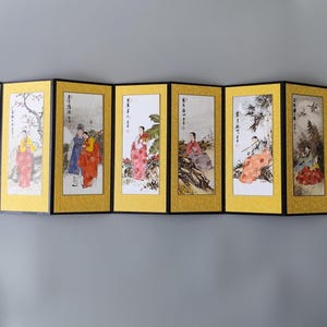 Puede incluir: Un biombo plegable de ocho paneles con bordes amarillos e inserciones rectangulares blancas. Cada panel muestra una ilustración distinta de tinta y acuarela de figuras con vestimenta tradicional, acompañada de texto caligráfico negro.