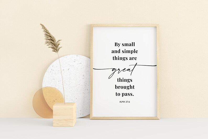 May include: A framed print with a white background and black text that reads "By small and simple things are great things brought to pass. ALMA 37:6". The print is sitting on a white surface with a wooden block and two round objects.