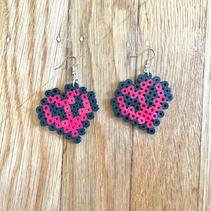 May include: A pair of heart-shaped earrings made with black and pink beads. The earrings are hanging from silver hooks.