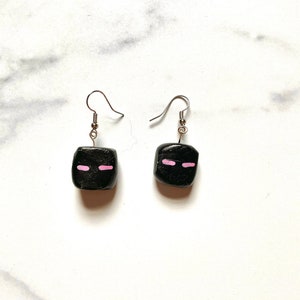 May include: A pair of black square earrings with pink painted eyes. The earrings have silver hooks.
