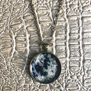 May include: A silver and blue resin pendant necklace with a bronze chain. The pendant is round and has a marbled design.