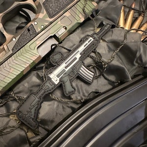 May include: An overhead shot features a camouflage-patterned handgun and a black and gray patch of a rifle. The patch is detailed with white accents. Several bullets are visible, along with a black magazine.