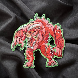 May include: Red and green embroidered patch of a cartoon monster with sharp teeth and claws.
