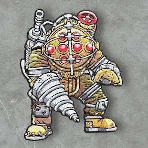 May include: A yellow and brown embroidered patch of a Big Daddy from the video game Bioshock. The Big Daddy is wearing a diving suit with a drill arm and a helmet with red lights.