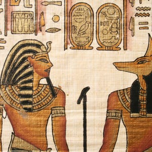May include: An Egyptian papyrus painting depicting a pharaoh and Anubis, the jackal-headed god. The pharaoh wears a striped headdress and gold accents. Anubis is shown with a black head and gold details. The background includes hieroglyphs and cartouches.
