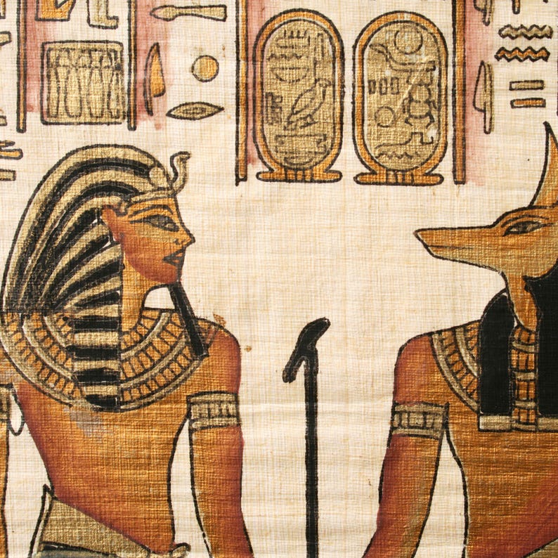 May include: An Egyptian papyrus painting depicting a pharaoh and Anubis, the jackal-headed god. The pharaoh wears a striped headdress and gold accents. Anubis is shown with a black head and gold details. The background includes hieroglyphs and cartouches.