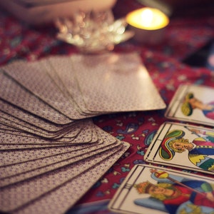 Pode incluir: Um close-up de um baralho de cartas de tar&ocirc; espalhado sobre uma toalha de mesa colorida com padr&otilde;es. As cartas t&ecirc;m um design roxo e branco.