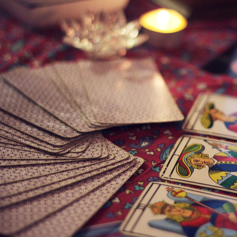 Pode incluir: Um close-up de um baralho de cartas de tar&ocirc; espalhado sobre uma toalha de mesa colorida com padr&otilde;es. As cartas t&ecirc;m um design roxo e branco.