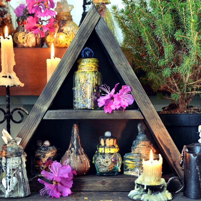 Pode incluir: Uma prateleira triangular de madeira com v&aacute;rias garrafas e frascos de vidro cheios de ervas e outros ingredientes. A prateleira &eacute; decorada com flores cor-de-rosa e velas.