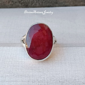 Könnte beinhalten: Ein silberner Ring mit einem großen, ovalen, tief roten Rubin-Edelstein.