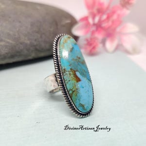Könnte beinhalten: Ein silberner Ring mit einem großen ovalen Türkis-Stein. Der Stein hat eine blaue und grüne Farbe mit braunen Adern. Der Ring hat ein seilartiges Design am Rand.