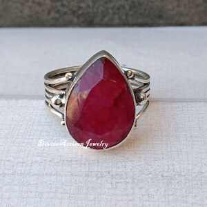 Könnte beinhalten: Ein silberner Ring mit einem tropfenförmigen Rubin-Edelstein. Der Ring hat ein strukturiertes Band mit kleinen silbernen Perlen.