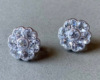 May include: A pair of silver flower-shaped earrings with clear cubic zirconia stones.