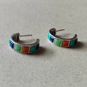May include: A pair of silver hoop earrings with a row of colourful stones. The stones are blue, green and orange.