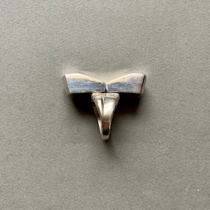 Op de afbeelding: Een zilveren ring met een uniek, geometrisch ontwerp. De ring is gemaakt van twee delen die in het midden aan elkaar zijn verbonden. De ring is een statement piece die perfect zou zijn voor een moderne bruid.