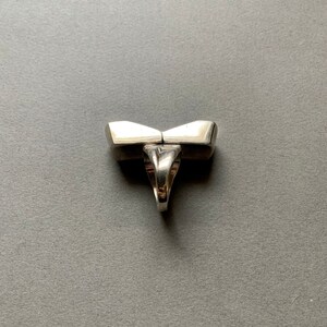 Op de afbeelding: Een zilveren ring met een uniek geometrisch ontwerp. De ring is gemaakt van twee delen die in het midden aan elkaar zijn verbonden. De ring is aan de onderkant open en heeft een gladde, gepolijste afwerking.