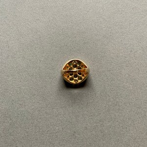May include: A gold ring with a rounded, oval face. The face of the ring is adorned with small, dark green gemstones arranged in a floral pattern. The band of the ring is a solid, polished gold.