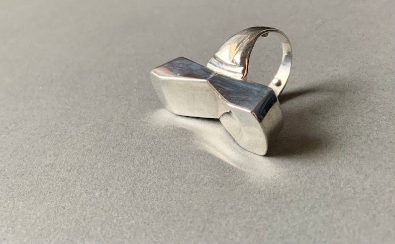 Op de afbeelding: Een zilveren ring met een geometrisch ontwerp. De ring is gemaakt van &eacute;&eacute;n stuk metaal en heeft een unieke, abstracte vorm.