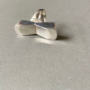 Op de afbeelding: Een zilveren ring met een geometrisch ontwerp. De ring is gemaakt van twee rechthoekige vormen die in het midden met elkaar verbonden zijn. De ring is een statement piece en zou een geweldige aanvulling zijn op elke sieradencollectie.
