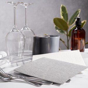 May include: Two gray cleaning cloths, one white cleaning cloth, two wine glasses, a gray mug, a gray and white mug, and a brown glass bottle with a pump dispenser on a white marble surface.