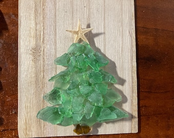 May include: A green glass Christmas tree made of sea glass with a starfish on top, mounted on a wooden background.