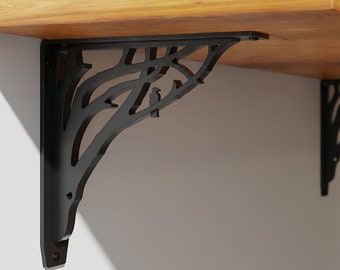 May include: Two black metal shelf brackets with a tree branch design. The brackets are attached to a wooden shelf with two framed pictures on top.