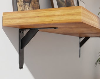 May include: A wooden shelf with black metal brackets. The shelf is mounted to a white wall and has two framed pictures on top.