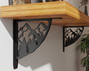 May include: Two black metal shelf brackets with a mountain and pine tree design. The brackets are attached to a wooden shelf with two framed pictures on top.