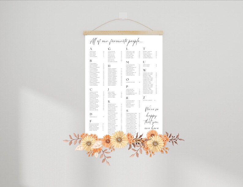 May include: A white poster with a seating chart for a wedding. The poster is hanging on a wall with a wooden frame and a rope. The poster has the text "All of our favourite people..." at the top and lists names in alphabetical order. The poster also has the text "We're so happy that you are here" at the bottom. The poster is decorated with orange and yellow flowers.