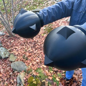 Op de afbeelding: Zwarte, bolvormige prop met hoekige accenten. De prop heeft een matte afwerking en wordt voor een natuurlijke achtergrond gehouden. Het ontwerp van de prop heeft een centrale diamantvorm en driehoekige punten.