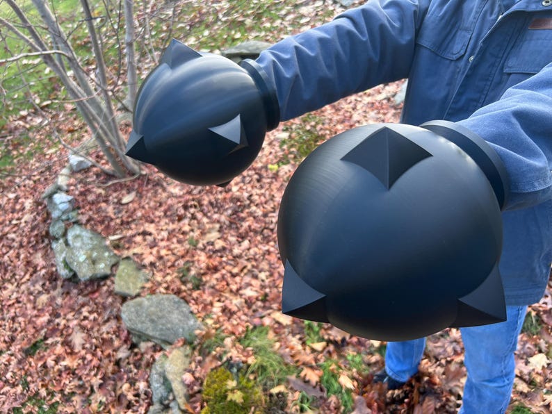 Op de afbeelding: Zwarte, bolvormige prop met hoekige accenten. De prop heeft een matte afwerking en wordt voor een natuurlijke achtergrond gehouden. Het ontwerp van de prop heeft een centrale diamantvorm en driehoekige punten.