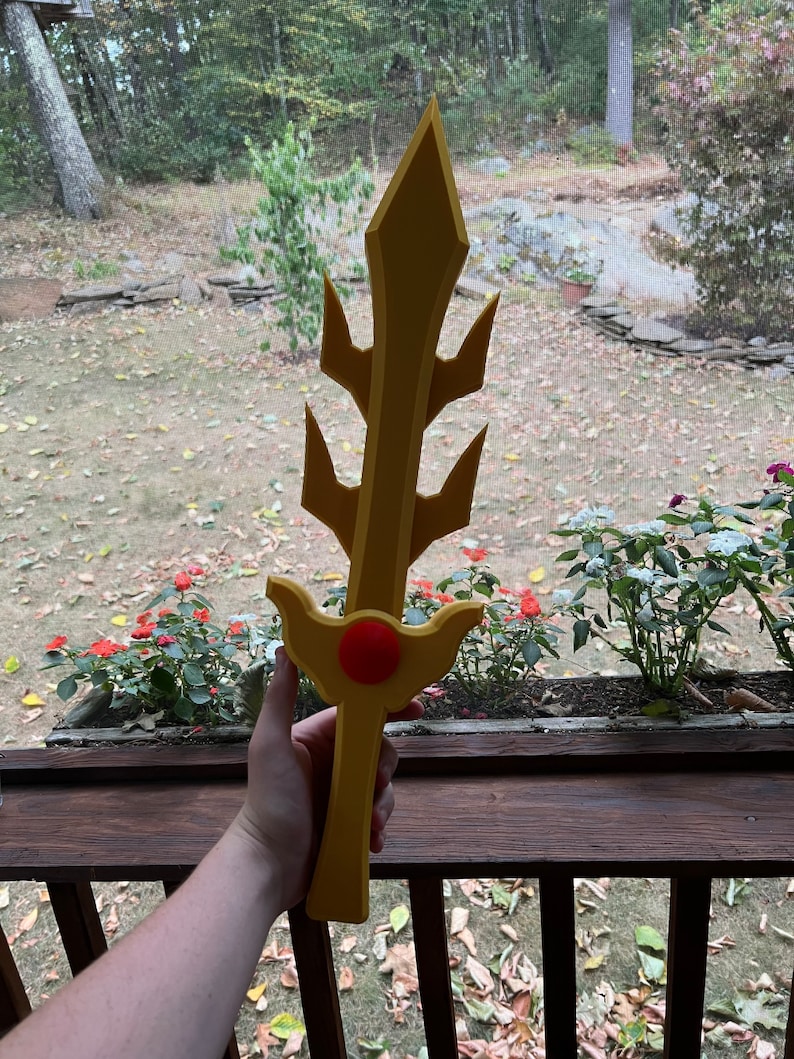 May include: A yellow foam sword with a red center and a pointed tip. The sword has a decorative design with multiple points.